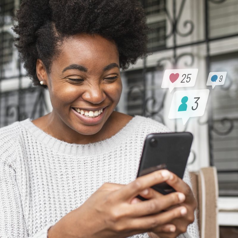 An african american woman holding up a phone and smiling at it to indicate how we prioritize mobile optimization in our web design agency